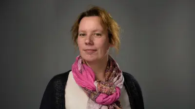 Britta trägt einen Schal, hat ihre roten Haare zusammengebunden und blickt in die Kamera.