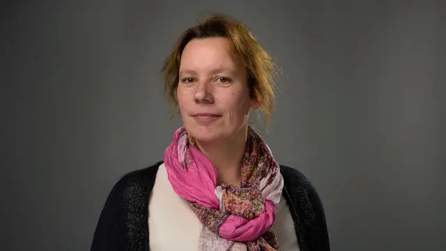 Britta trägt einen Schal, hat ihre roten Haare zusammengebunden und blickt in die Kamera.