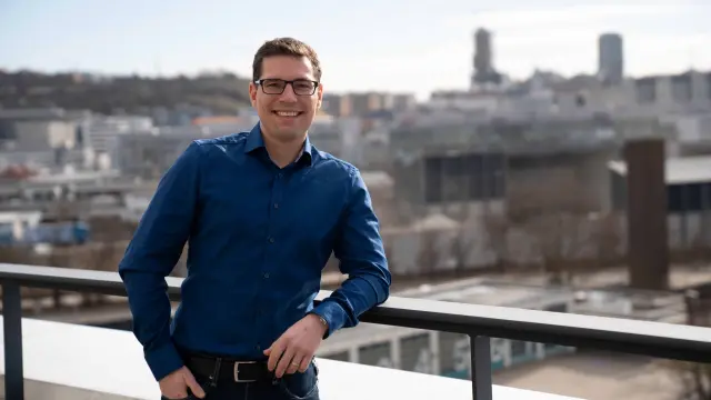 Michael lehnt am Geländer einer Dachterrasse und lächelt in die Kamera.
