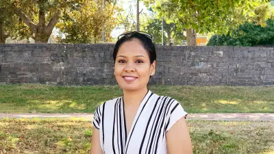 Swathi steht draußen im Grünen vor einer Mauer und lächelt in die Kamera.