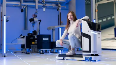 Junge Frau auf Rollwagen vor einem Industrieroboter