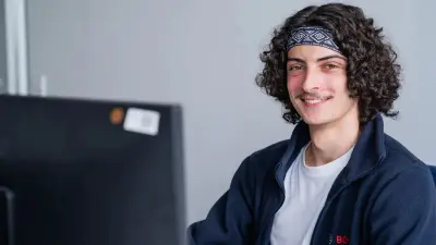 Auszubildender lacht in die Kamera und sitzt vor einem PC