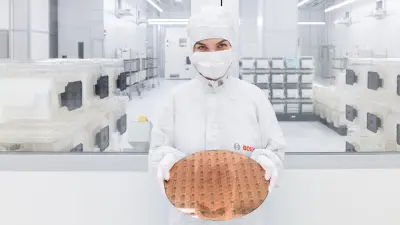 Mitarbeiterin in Reinraumkleidung hält einen Silizium-Wafer in einer hochmodernen Produktionsumgebung