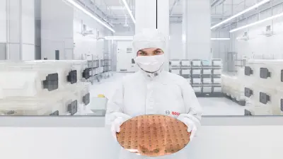 Mitarbeiterin in Reinraumkleidung hält einen Silizium-Wafer in einer hochmodernen Produktionsumgebung