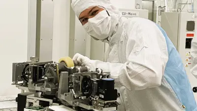 Mitarbeiter im Reinraum montiert eine hochpräzise Maschine in einer Halbleiterfertigung und arbeitet konzentriert an der Anlage.