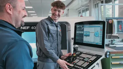 Azubi und Ausbilder bei Bosch Lollar bedienen gemeinsam eine CNC-Maschine und lachen im Gespräch.