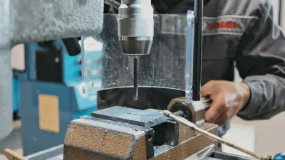Nahaufnahme einer Bohrmaschine in der Bosch-Ausbildung, ein Azubi spannt ein Werkstück unter dem Bohrer ein.