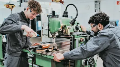 Zwei Auszubildende arbeiten konzentriert an einer grünen Fräsmaschine in der Bosch-Werkstatt in Lollar.