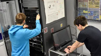Fachinformatik-Auszubildende arbeiten gemeinsam an einem Serverschrank.