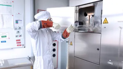 Ein Auszubildender der Mikrotechnologie bei Bosch im Reinraumanzug belädt ein Quarzboot mit Silizium-Wafern in einen Oxidationsofen.
