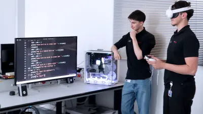 Zwei Auszubildende der Fachinformatik lernen gemeinsam; einer trägt eine VR-Brille, beide schauen sich die Ergebnisse am PC an.
