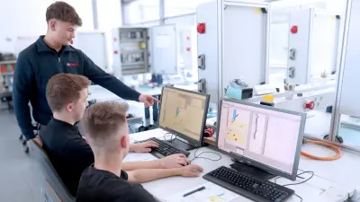 Drei Auszubildende in der Mechatronik bei Bosch lernen gemeinsam an Desktop-PCs in einer Büroumgebung.
