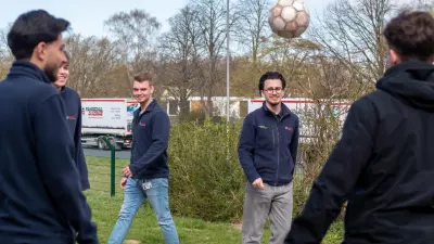Mehrere Auszubildende spielen in ihrer Pause Fußball auf einem Outdoor-Basketballfeld. Sie lachen, bewegen sich aktiv und genießen das Miteinander an der frischen Luft.