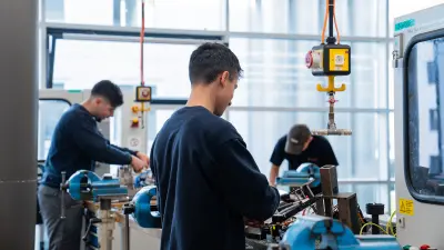 Drei Auszubildende stehen an einer Werkbank und üben an elektronischen Komponenten.