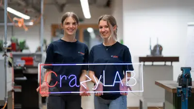 Zwei Ausbildende halten ein leuchtendes Schild mit "CrazyLab".