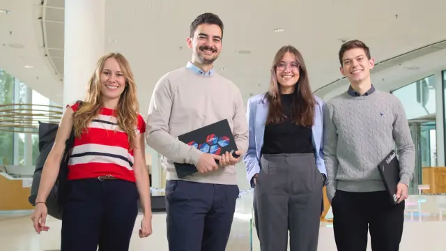 Vier junge Menschen stehen nebeneinander und lächeln in die Kamera.