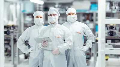 Drei Personen in weißen Schutzanzügen in einer Produktionshalle.