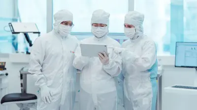 Drei Personen in weißen Schutzanzügen stehen in einem Labor und betrachten gemeinsam ein Tablet.