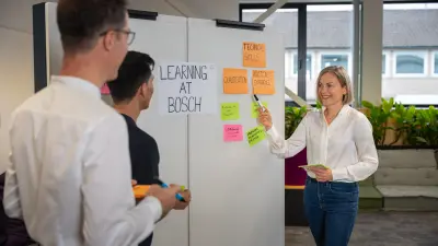 Eine Mitarbeiterin klebt nach Rücksprache mit ihren Kollegen Post-its an eine Wand