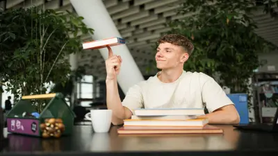 Student der ein Buch auf dem Finger balanciert