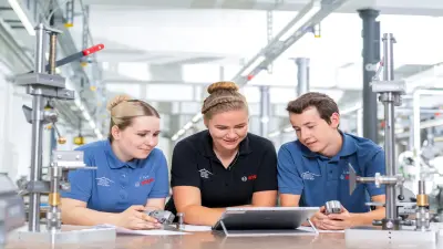 Drei Auszubildende in der Werkstatt schauen auf einen Laptop-Bildschirm