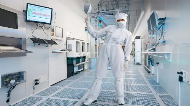 Frau im Laboranzug hält einen Mikrochip hoch