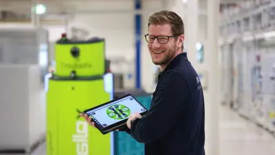 Lächelnder Mitarbeiter steuert fahrerloses Transportsystem mit Tablett.