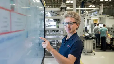 Mitarbeiterin in Fertigungshalle bedient Touchscreen.