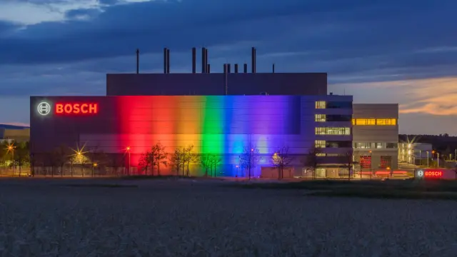 Bunte Scheinwerfer lassen das Bosch Werk in der Dämmerung in Regenbogenfarben erstrahlen.