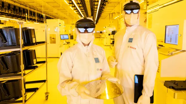 Eine Frau, die einen Wafer hält, und ein Mann stehen in weißer Schutzkleidung im Reinraum.