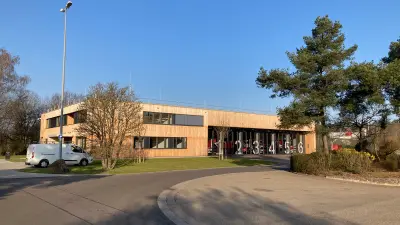 Feuerwehrgebäude auf Werksgelände mit Fahrzeugstellplätzen und Holzfassade.