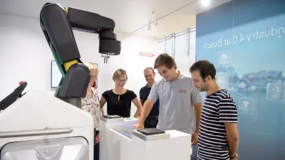 Auszubildende bedienen einen Industrieroboterarm über ein Steuergerät im Bosch Werk Homburg