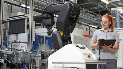 Eine Auszubildende mit einem Steuergerät für einen Industrierobotorarm im Bosch Werk Homburg