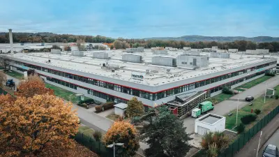 Luftaufnahme eines Industriegebäudes mit umliegenden Straßen und Bäumen.