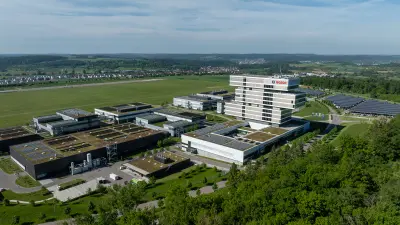 Luftaufnahme eines weitläufigen Forschungscampus, bestehend aus mehreren modernen Gebäuden mit Flachdächern, teils mit Solarpaneelen. In der Mitte ragt ein mehrstöckiger Turm hervor.