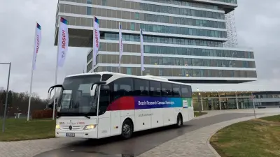 Ein großer weißer Shuttle‑Bus mit Bosch‑Branding steht vor einem modernen Bürogebäude mit auskragendem Obergeschoss.