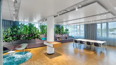 Ein moderner und heller Raum in einem Bürogebäude von Bosch Sensortec in Kusterdingen mit bodentiefen Fenstern, Pflanzen und mehreren Sitzgelegenheiten.