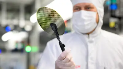 Ein Mann in einem weißen Reinraumoverall und weißer Maske betrachtet einen Halbleiter-Wafer.