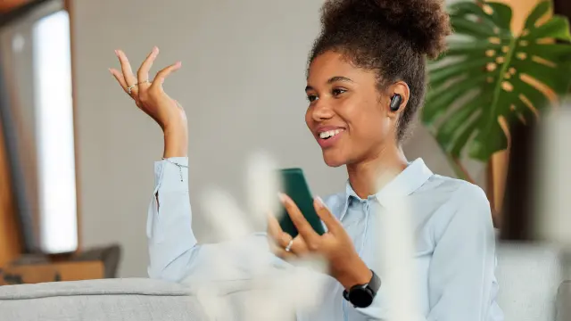 Eine Frau sitzt auf einer Couch und hält ein Telefon in der Hand.