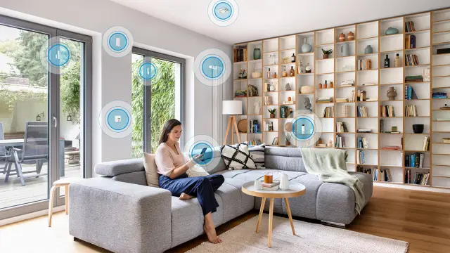 Frau sitzt mit ihrem Handy auf dem Sofa und steuert damit smart das Wohnzimmer.