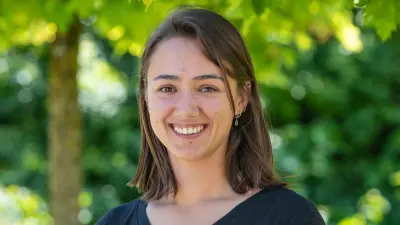 Chiara steht lächelnd vor Bäumen im Grünen und blickt in die Kamera. Sie ist bis zum Oberkörper zu sehen.