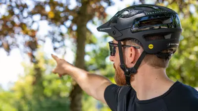 Kevin hat einen Fahrradhelm sowie eine Sonnenbrille an und zeigt in Richtung Wald.