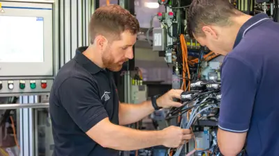 Kevin ist mit einem Kollegen in der Fertigung und schaut sich mit ihm gemeinsam die Kabel einer Maschine genauer an.