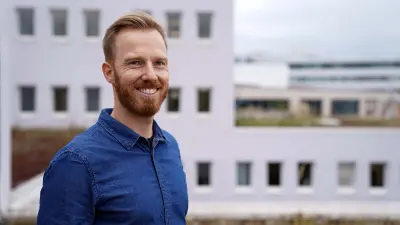Porträt von Christoph Dörr, der ein blaues Jeanshemd trägt, draußen steht und freundlich in die Kamera lächelt.