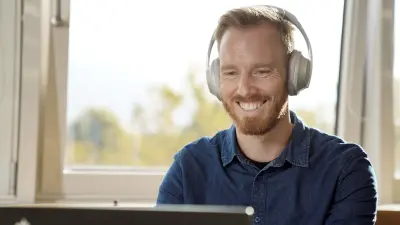 Christoph Dörr sitzt an seinem PC, trägt Kopfhörer und lächelt. Hinter ihm sieht man ein gekipptes Fenster.
