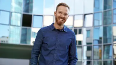 Christoph Dörr steht vor einer Fensterfront, trägt ein blaues Jeanshemd und lächelt in die Kamera.