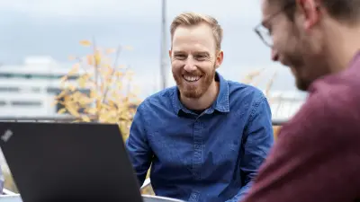 Christoph Dörr sitzt gemeinsam mit einem Kollegen draußen an einem Tisch und richtet seinen freundlichen Blick auf den vor ihm stehenden Laptop.