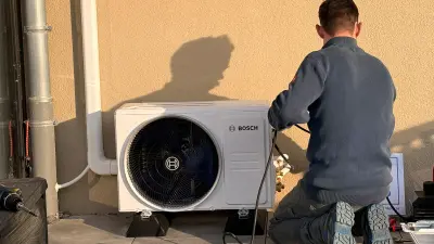 Ein Handwerker installiert eine Klimagerät an der Außenwand eines Gebäudes.