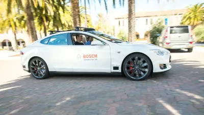 Ein weißes von Bosch gebrandetes Auto, von der Seite zu sehen, zwei Männer sitzen im Auto. 