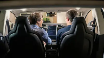 Moritz Dechant und ein junger Mann sitzen in einem Auto. Sie sind von hinten zu sehen. Man schaut durch die Windschutzscheibe. 